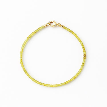 A studio hero shot of a 2mm natural faceted peridot cube bead bracelet with a 14K gold-filled clasp, showcasing the light-catching geometric facets and bright green clarity.
