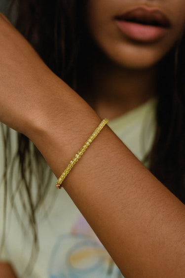 A lifestyle shot of a model wearing a dainty 2mm faceted peridot cube bracelet, highlighting the vibrant apple-green gemstone sparkle against a casual green outfit.

