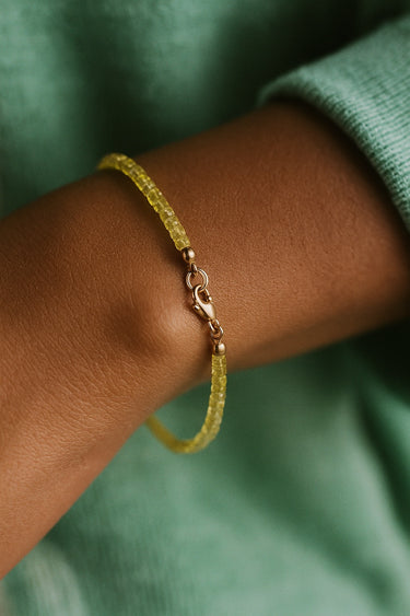 A close-up lifestyle view of the 2mm peridot cube bracelet on a model's wrist, emphasizing its delicate minimalist silhouette and modern artisanal quality.
