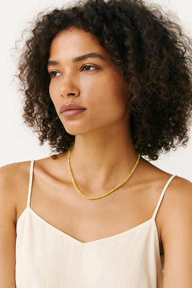 A portrait of a woman wearing the 2mm peridot cube necklace, showcasing its sophisticated minimalist silhouette and clean, architectural edge.
