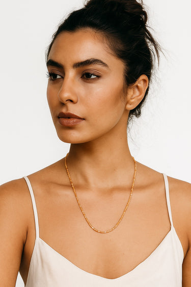A woman wearing the 2mm golden sunstone cube necklace, highlighting its editorial, sophisticated silhouette and the fine texture of the faceted beads.
