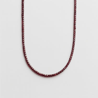 A professional studio hero shot of the women's 3mm faceted garnet cube necklace arranged in a U-shape against a neutral background, highlighting the geometric precision and deep red color of the stones.
