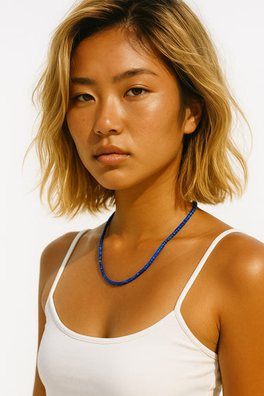 A lifestyle shot of a woman wearing the 3mm faceted Lapis Lazuli cube necklace against a white top, showcasing the vibrant blue color and clean architectural drape.
