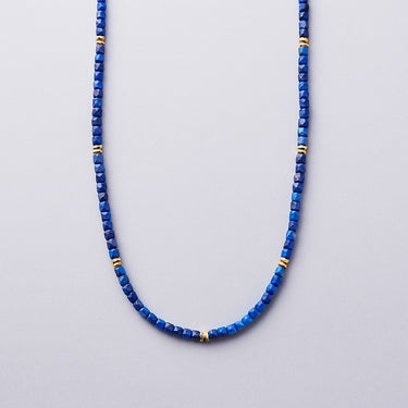 A 3mm faceted Lapis Lazuli cube bead necklace with 14K gold-filled spacer accents, arranged in a clean U-shape against a neutral background.
