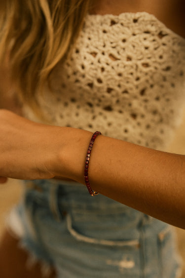 A lifestyle shot of a model wearing a dainty 3mm faceted garnet cube bracelet, showcasing its delicate sparkle and sophisticated, minimalist silhouette.
