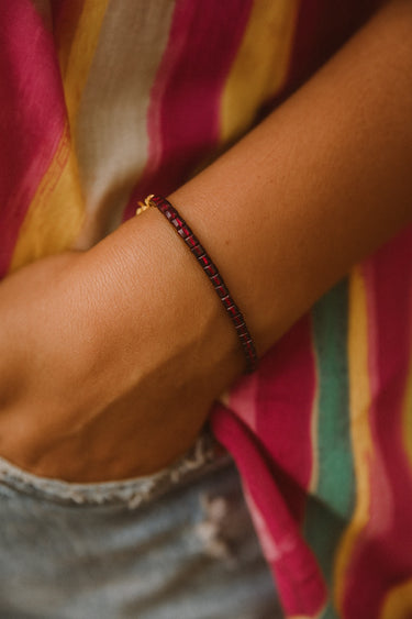 A lifestyle view of the 3mm faceted garnet cube bracelet on a model wearing a vibrant striped top, demonstrating its versatility as a refined everyday luxury staple.

