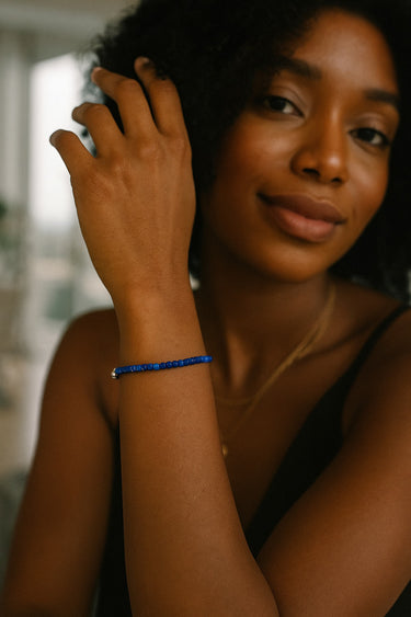 A lifestyle portrait of a model wearing a dainty 3mm faceted lapis lazuli cube bracelet, showcasing its sophisticated sparkle and minimalist silhouette in a soft indoor setting.
