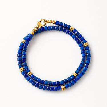 A studio hero shot of a women's 3mm natural faceted lapis lazuli cube wrap bracelet featuring 14K gold-filled bead accents, highlighting the vibrant royal blue gemstones and elegant layered design.

