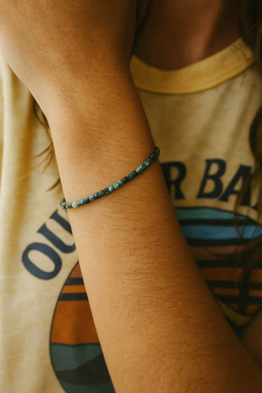 A lifestyle view of the 3mm faceted tourmaline cube bracelet on a model’s wrist, emphasizing its delicate artisanal quality and rich, natural color palette.
