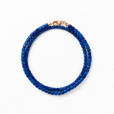 A studio hero shot of a women's 3mm natural lapis lazuli wrap bracelet featuring 14K gold-filled bead accents, showcasing the vibrant royal blue stones and elegant double-layered design.
