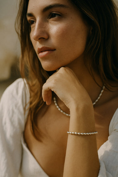 A lifestyle shot of a model wearing the 3mm sterling silver oval rice chain bracelet paired with a matching necklace, demonstrating its sophisticated drape and architectural influence.
