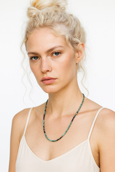 A woman wearing the 3mm faceted tourmaline cube necklace, highlighting the delicate scale and architectural form of the dark green and teal gemstones.
