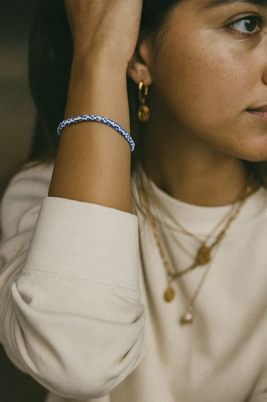 A lifestyle image of a model wearing the 3mm vintage African chevron bead bracelet stacked with gold chains, demonstrating its architectural versatility and modern luxury aesthetic.
