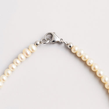 A macro detail shot of 4-5mm freshwater pearls meeting professional-grade sterling silver hardware, featuring a high-polish lobster clasp.
