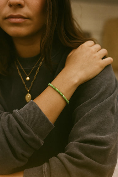 A lifestyle shot of a model wearing a women's 4mm African green chrysoprase heishi bead bracelet, showcasing the vibrant natural apple-green hues and its effortless, stackable silhouette.
