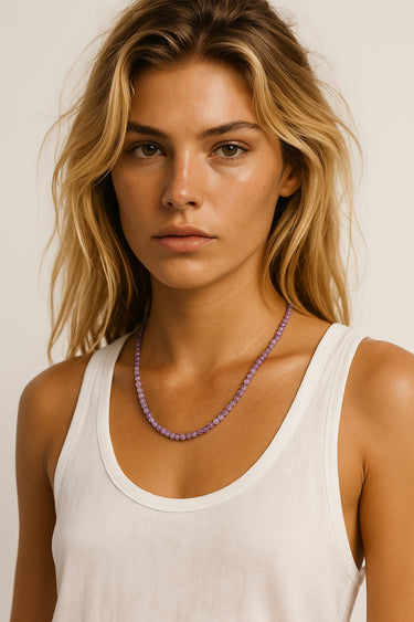 A model wearing a 4mm amethyst round bead necklace, showcasing the vibrant purple stones against a white tank top for an editorial, sophisticated look.
