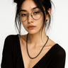 A lifestyle shot of a female model wearing a 4mm Black Lava heishi bead necklace, showcasing its tactile matte surface and sleek, minimalist profile.

