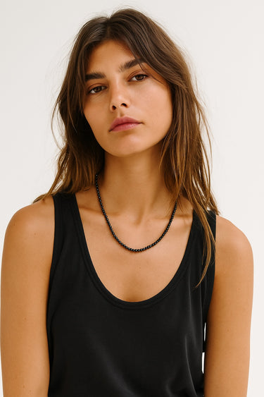 A woman wearing the 4mm gloss black onyx necklace against a black tank top, showcasing the subtle play of light on the polished stone surfaces.

