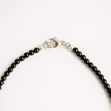 A close-up detail of a women's 4mm gloss black onyx necklace meeting professional-grade sterling silver hardware, featuring a secure lobster clasp.
