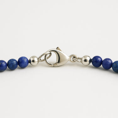 A macro detail of 4mm lapis lazuli beads meeting professional-grade sterling silver hardware, featuring a high-polish lobster clasp
