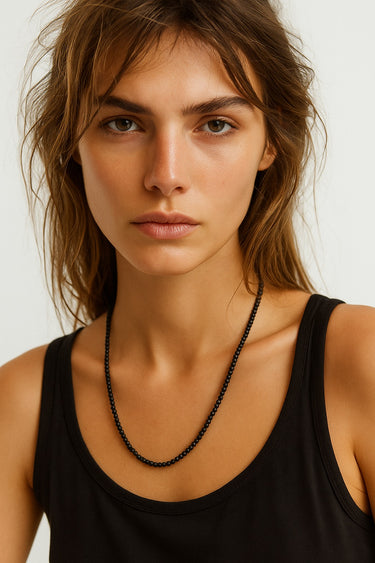 A woman wearing the 4mm matte black onyx necklace against a black tank top, showcasing the sophisticated velvet finish and clean architectural drape of the stones.
