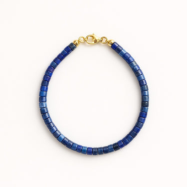 A studio hero shot of a women's 4mm natural lapis lazuli heishi bead bracelet with a 14K gold-filled clasp, highlighting the deep royal blue gemstone tones and sleek disk shape.
