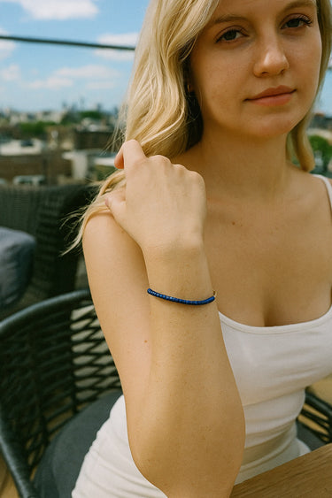A lifestyle portrait featuring the dainty 4mm lapis lazuli heishi bracelet, demonstrating its versatile design as a refined everyday luxury accessory.
