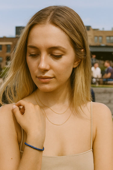 A lifestyle shot of a model wearing a 4mm lapis lazuli heishi bracelet, showcasing its sophisticated minimalist silhouette and vibrant blue color in a soft-focus outdoor setting.
