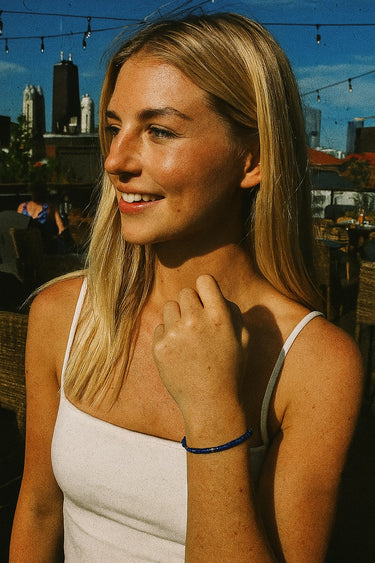A lifestyle view of the 4mm lapis lazuli heishi bracelet on a model’s wrist in bright sunlight, emphasizing the natural gemstone texture and elegant 14K gold-filled details.
