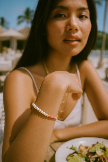 A lifestyle image of a model wearing a dainty pearl and rhodonite bracelet, showcasing its elegant luster and effortless drape for a sophisticated, everyday luxury look.
