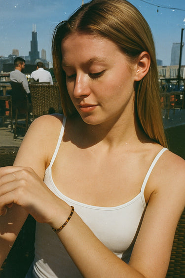 A lifestyle shot of a model wearing a 4mm tiger's eye heishi bracelet in natural sunlight, showcasing the warm golden tones and its effortless, stackable silhouette.
