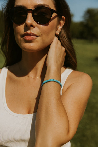 A lifestyle view of the 4mm turquoise heishi bracelet on a model’s wrist in natural light, demonstrating its effortless drape and timeless appeal as a modern jewelry staple.
