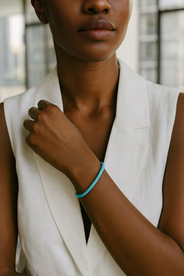 A lifestyle shot of a model wearing a women's 4mm natural turquoise heishi bead bracelet, highlighting the vibrant robin's egg blue stone tones and its refined, stackable silhouette.

