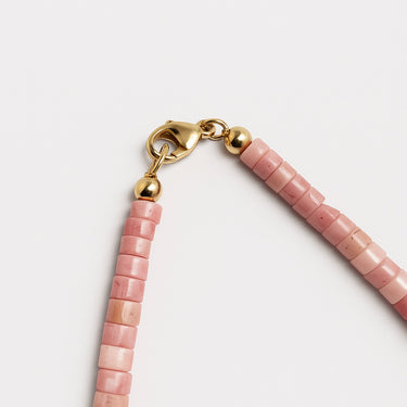 A close-up of a 14K gold-filled lobster clasp closure on a pink petrified rhodonite heishi necklace.
