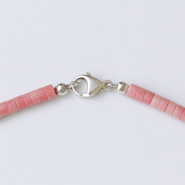 A close-up of a high-polish sterling silver lobster clasp closure on a pink petrified rhodonite heishi necklace.
