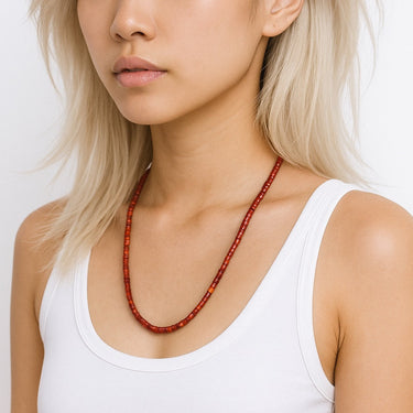 A lifestyle shot of a woman wearing the 4mm red agate heishi necklace against a white tank top, showcasing the bold color and clean architectural drape.
