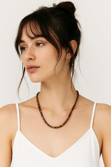 An editorial lifestyle portrait of a woman wearing the 4mm Tiger's Eye heishi necklace, highlighting the piece's structural presence and natural stone texture.
