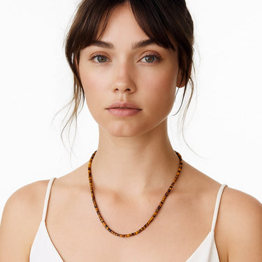 A lifestyle shot of a woman wearing the 4mm Tiger's Eye heishi necklace, showcasing the warm brown tones and clean architectural drape against a white top.
