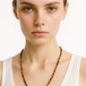 A lifestyle shot of a model wearing a 4mm Tiger’s Eye round bead necklace against a white tank top, showcasing its warm earth tones and refined drape.
