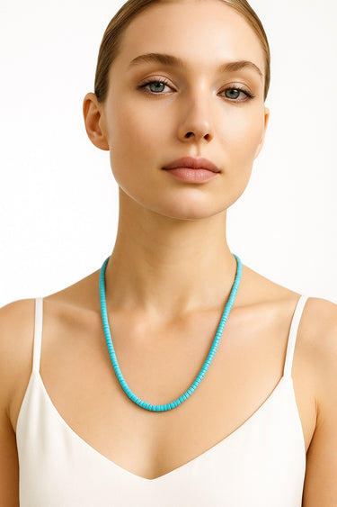 A lifestyle shot of a model wearing the 4mm Blue Turquoise heishi necklace against a white tank top, demonstrating its refined presence and natural drape.
