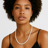 A lifestyle shot of a woman wearing the 4mm white turquoise heishi necklace against a black top, showcasing the bright white stones and clean architectural drape.
