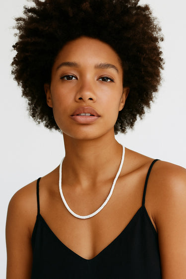 A lifestyle shot of a woman wearing the 4mm white turquoise heishi necklace against a black top, showcasing the bright white stones and clean architectural drape.
