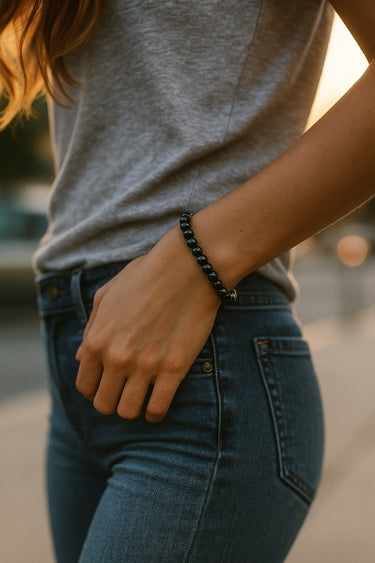 A lifestyle shot of a model wearing a women's 6mm gloss black onyx bead bracelet with a sterling silver accent, showcasing the high-shine reflective surface of the stones.
