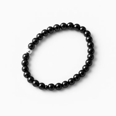 A top-down studio shot of the 6mm gloss black onyx bracelet with a silver accent bead, emphasizing the architectural symmetry and polished luster of the semi-precious stones.
