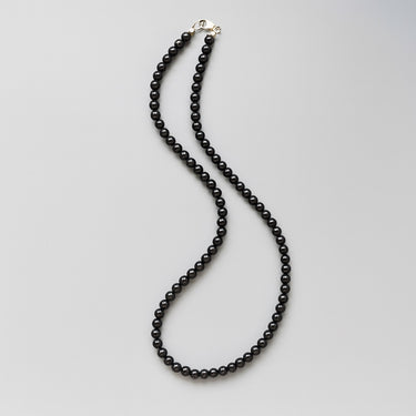 A studio shot of the 6mm gloss onyx necklace in a fluid S-curve, highlighting the rhythmic pattern and high-end tactile finish of the polished gemstones.
