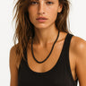 A lifestyle shot of a woman wearing the 6mm gloss onyx necklace against a black tank top, showcasing the mirror-like polish of the black stones and a clean architectural drape.
