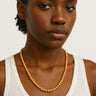 A lifestyle shot of a model wearing a 6mm Golden Sandalwood round bead necklace against a white tank top, showcasing its warm honey tones and natural drape.
