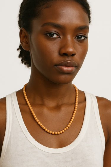 A lifestyle shot of a model wearing a 6mm Golden Sandalwood round bead necklace against a white tank top, showcasing its warm honey tones and natural drape.
