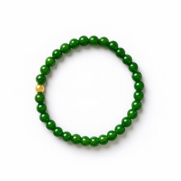 A studio hero shot of a women's 6mm green jade bead bracelet featuring a single 14K gold-filled accent bead, arranged in a clean circular form to highlight the natural stone luster and architectural contrast.
