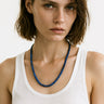 A lifestyle shot of a female model wearing a 6mm Lapis Lazuli round bead necklace against a white tank top, showcasing its deep blue color and elegant drape.
